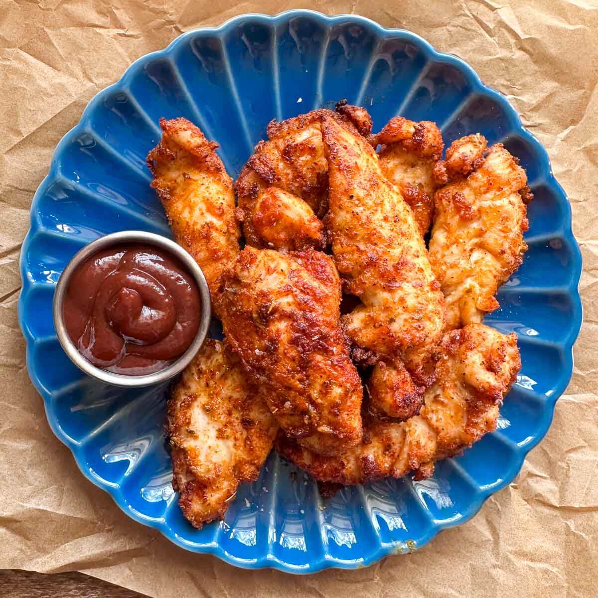 air fryer chicken tenders on blue plate with container of bbq sauce on the side
