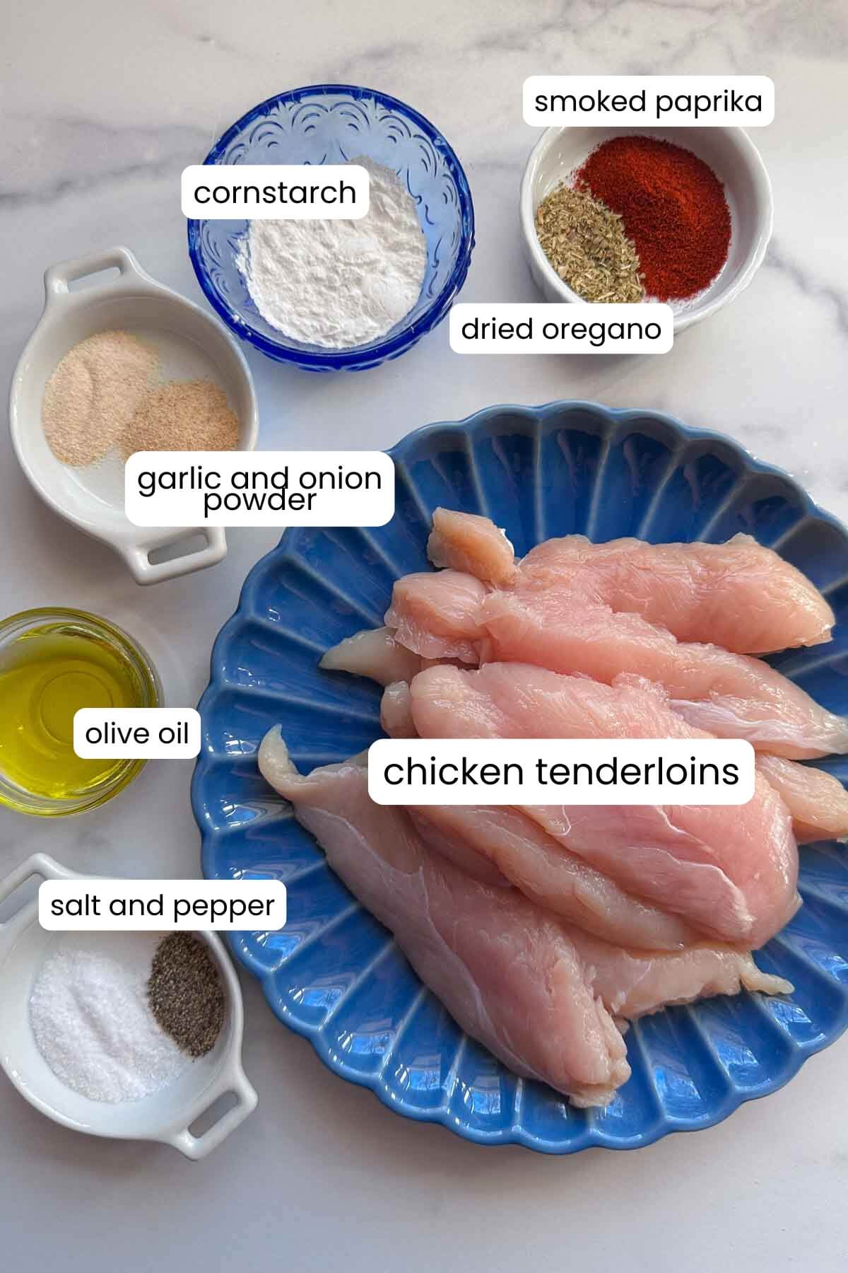 ingredients for air fryer chicken tenderloins: small bowls of spices, cornstarch, and olive oil. blue plate with raw chicken tenderloins 