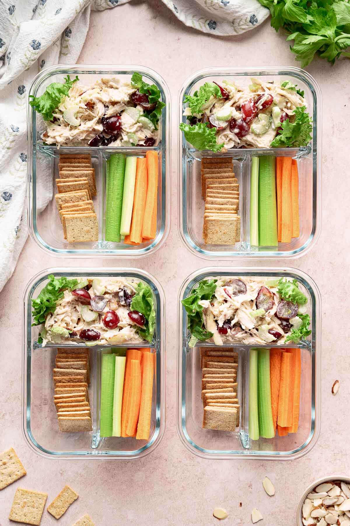 Chicken salad with grapes packed into glass meal prep containers with crackers and fresh vegetables for easy lunches.