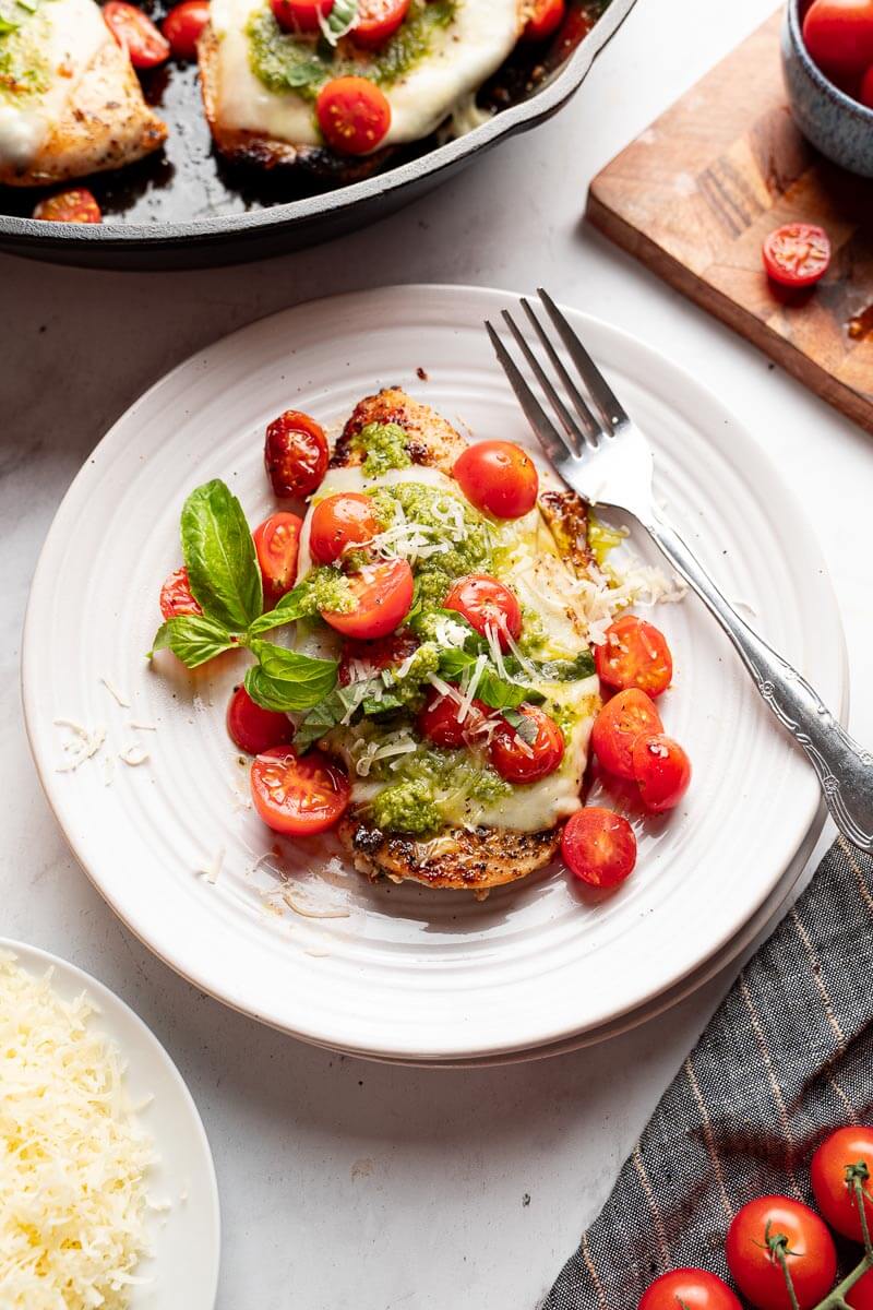 grilled chicken margherita on white plate with pesto mozzarella and cherry tomatoes