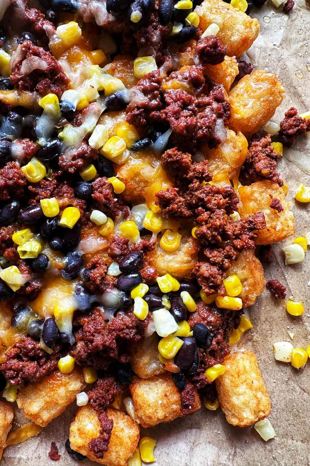 Tater tots topped with taco seasoned ground beef, black beans, corn, and melted cheese on a baking sheet