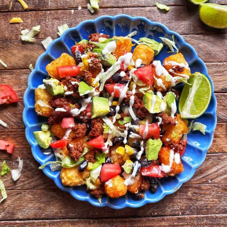 Loaded totchos made with crispy tater tots, seasoned ground beef, cheese, black beans, corn, avocado, and sour cream