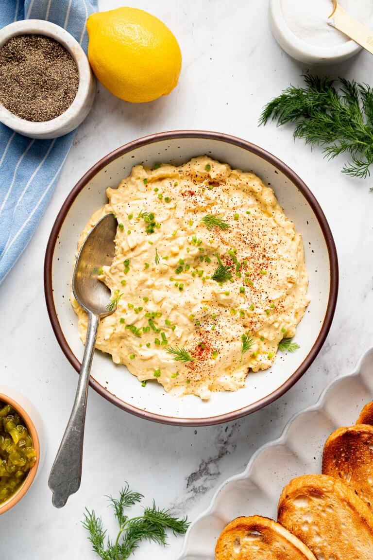 cottage cheese egg salad in bowl with spoon surrounded by toasted bread, fresh dill, and a lemon