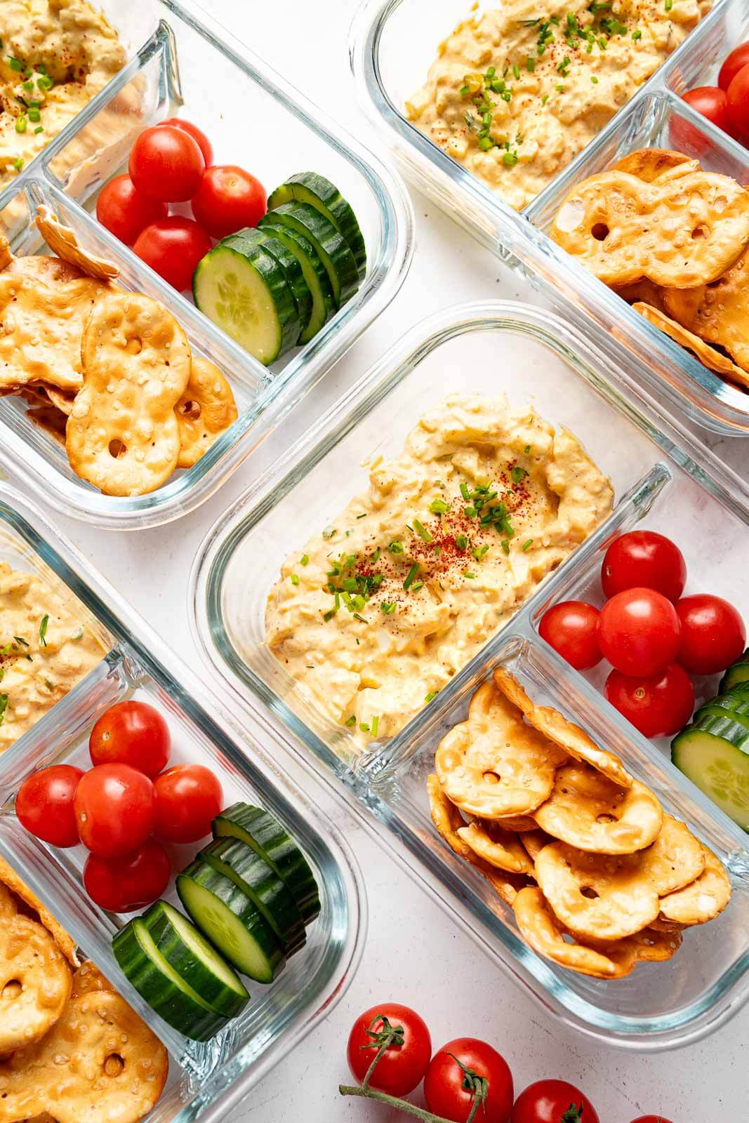 cottage cheese egg salad in meal prep containers with pretzels, cherry tomatoes, and slices of cucumber