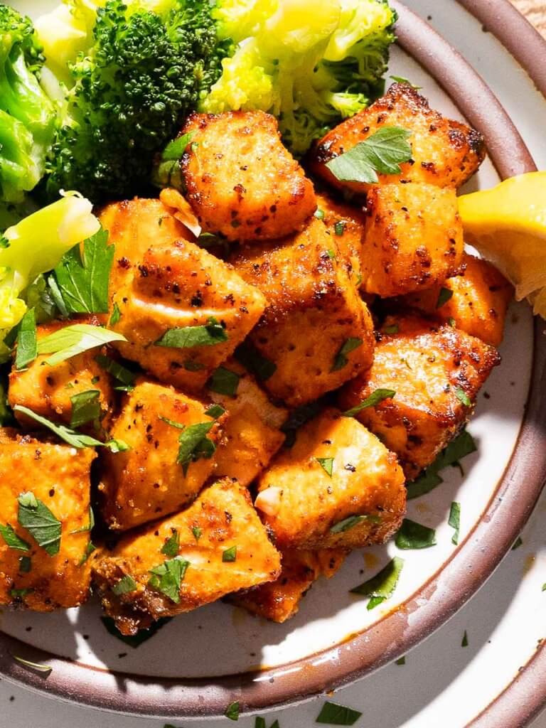 Crispy air fryer salmon bites with broccoli and lemon on a plate.
