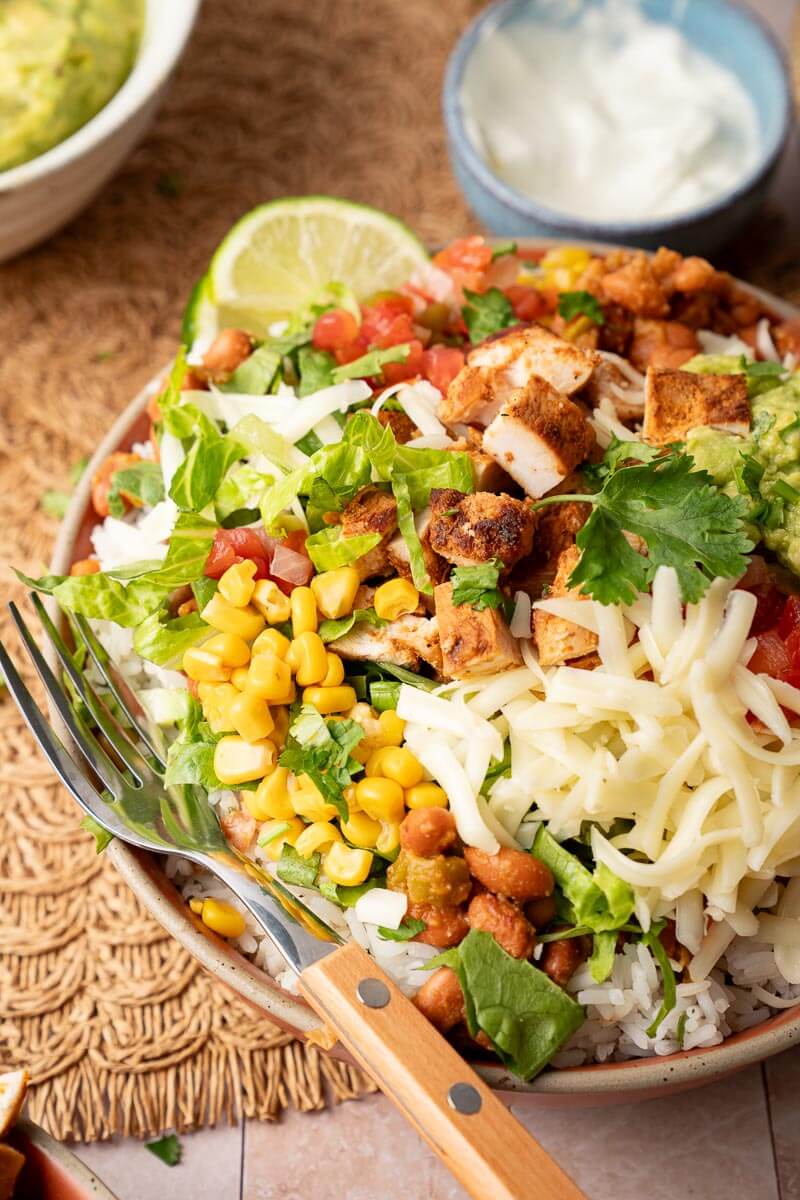 chicken burrito bowl with lettuce, cheese, corn, pinto beans, chicken, and rice