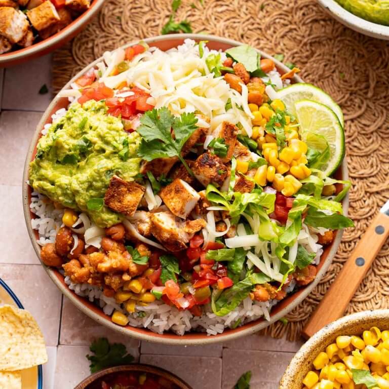 Chipotle chicken burrito bowl with rice, pinto beans, corn, pico de gallo, guacamole, cheese, and lettuce
