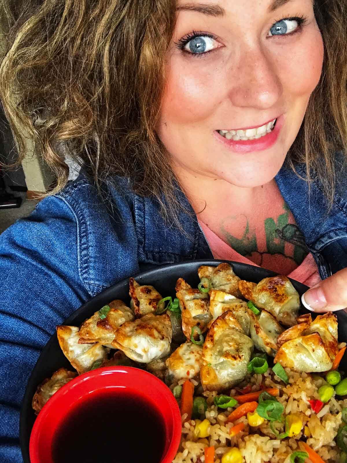 Star Anastasia holding a plate of dumplings and chicken fried rice.