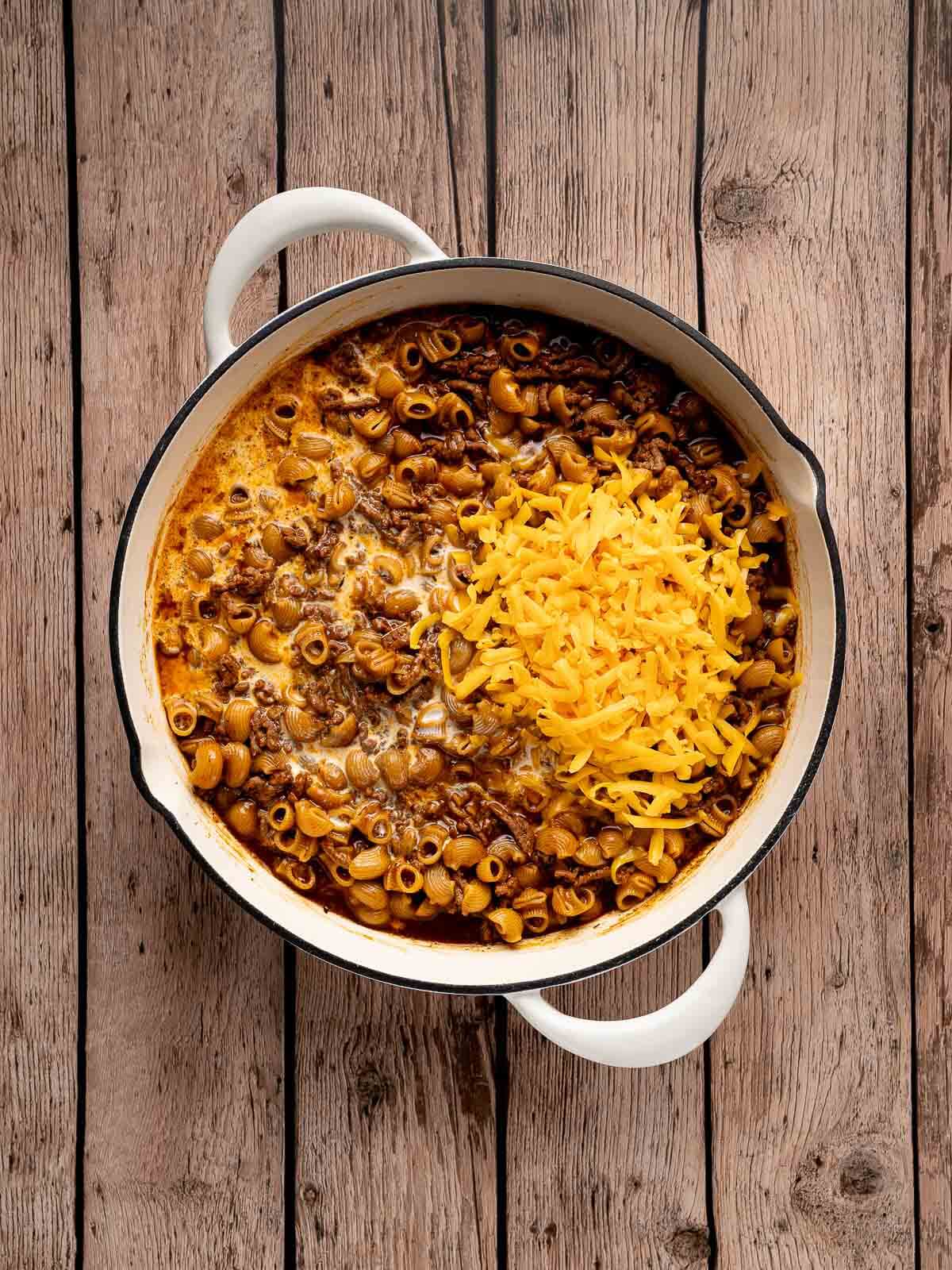 a large skillet filled with sauce-y pasta, ground beef, and shredded cheddar cheese.