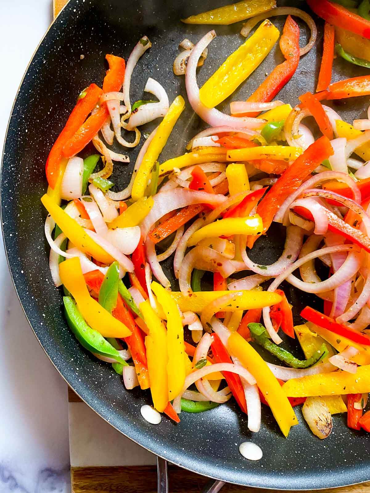 sliced bell peppers and onions in a skillet cooking.
