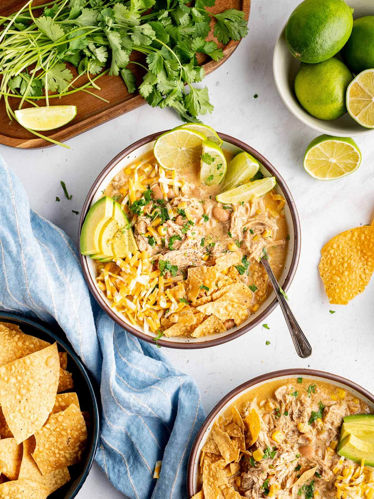 bowl of creamy chicken chili with cilantro, limes, and tortilla chips. 