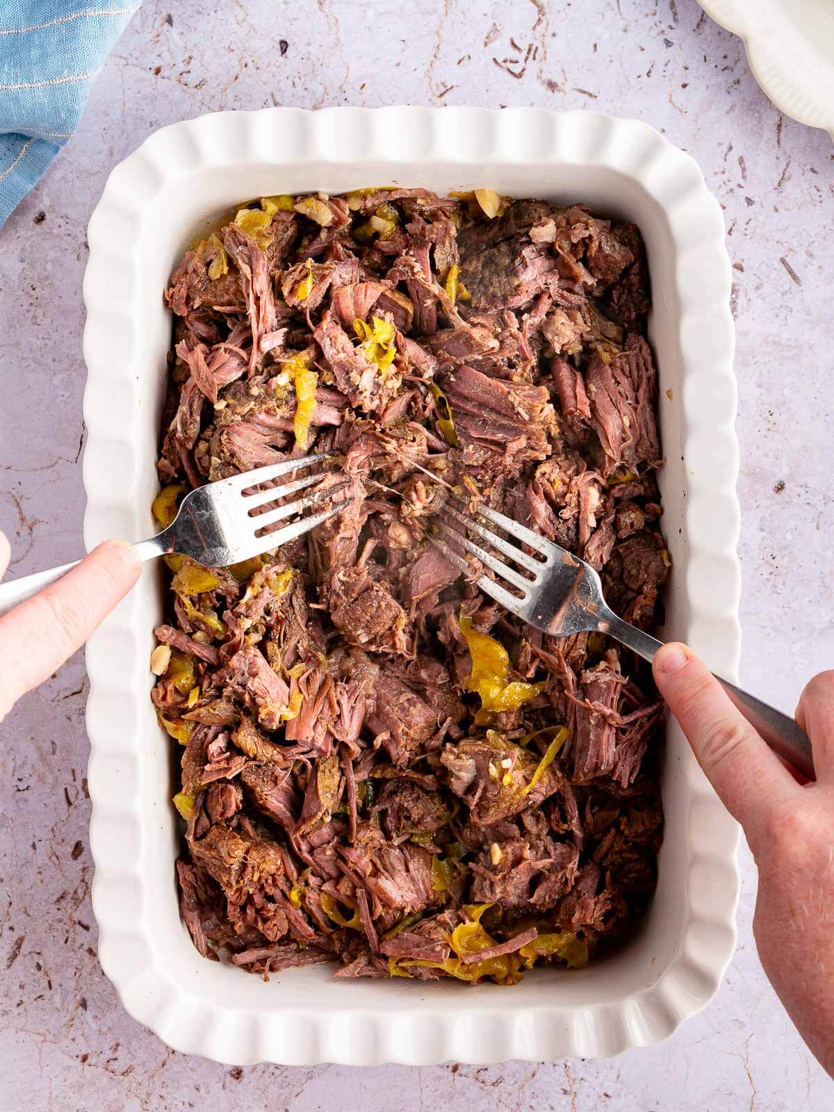 beef in a casserole dish being shredded.