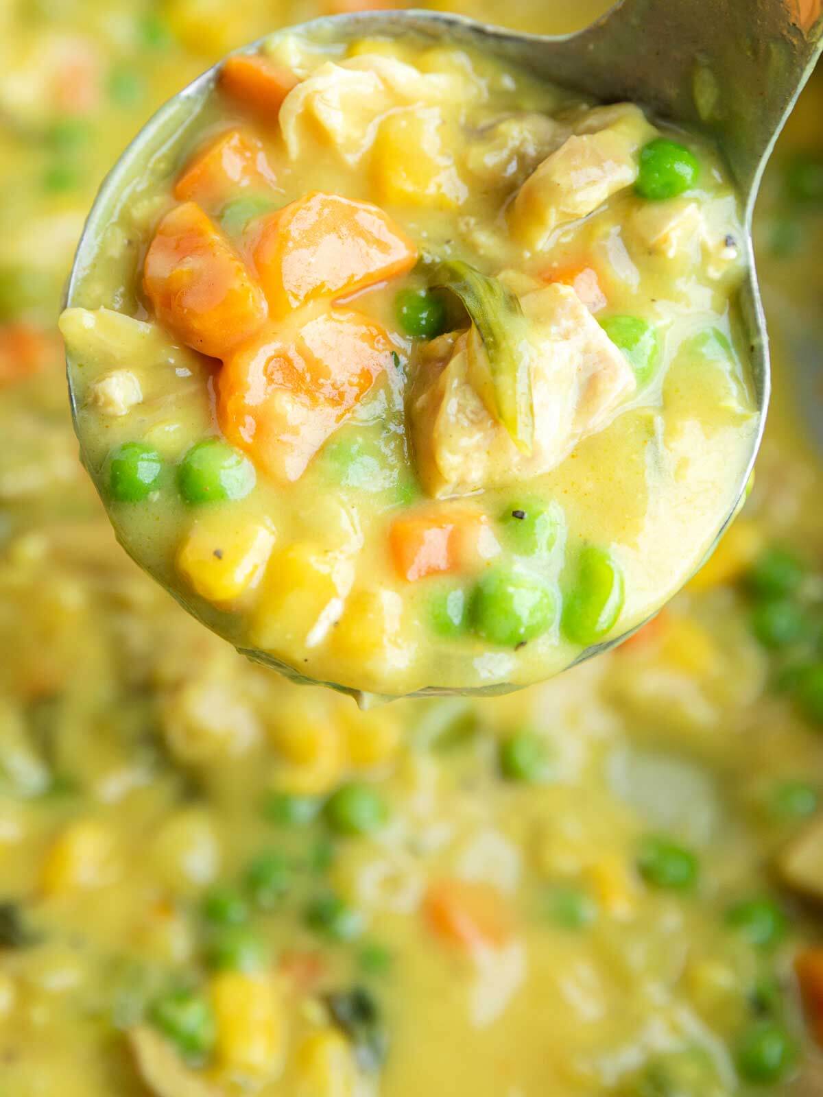Ladle filled with thick and creamy chicken pot pie soup, chicken, carrots, peas, and corn.