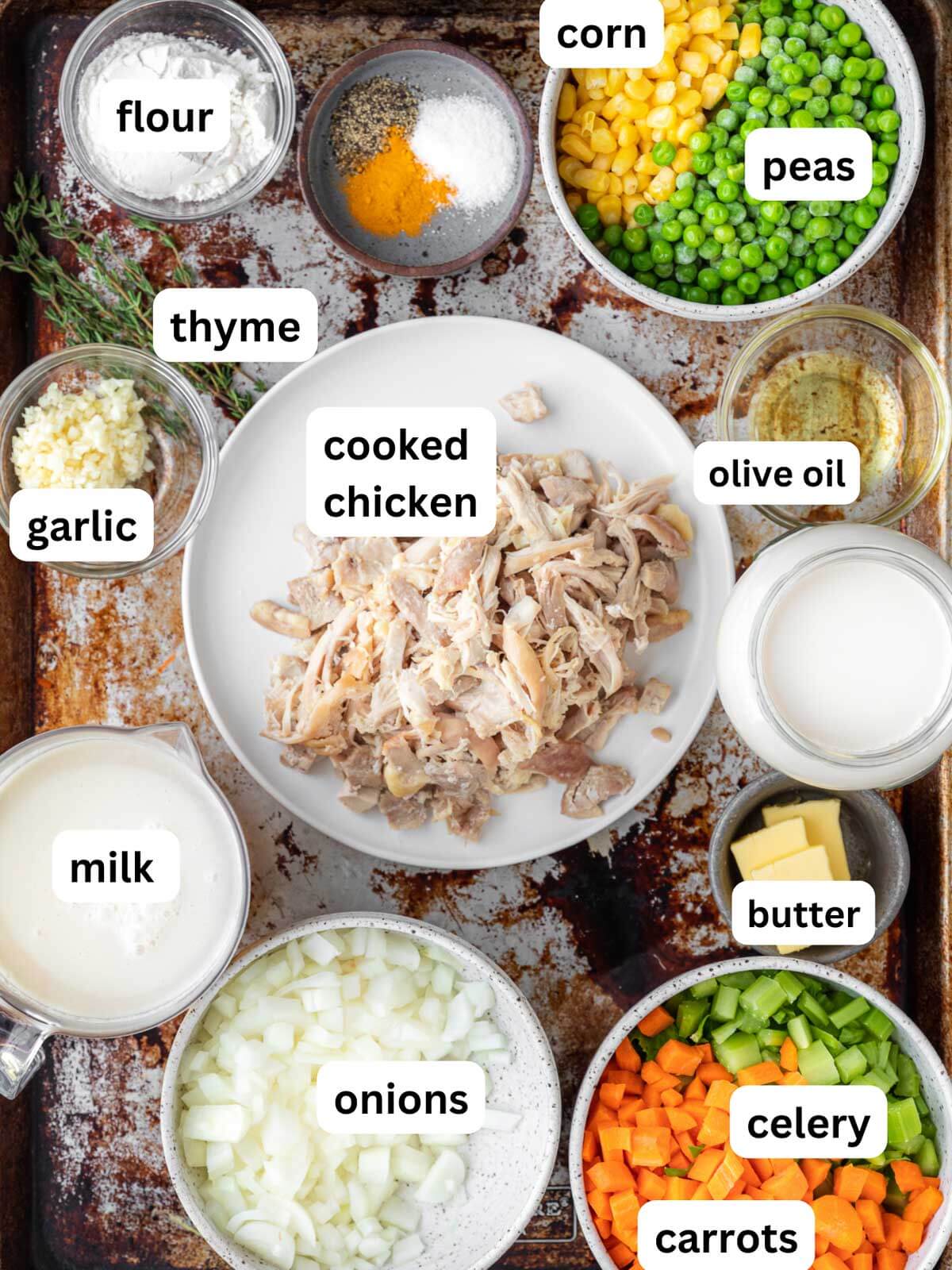 bowls of ingredients: flour, spices, peas, corn, garlic, cooked and shredded chicken, carrots, celery, diced onion, and milk.