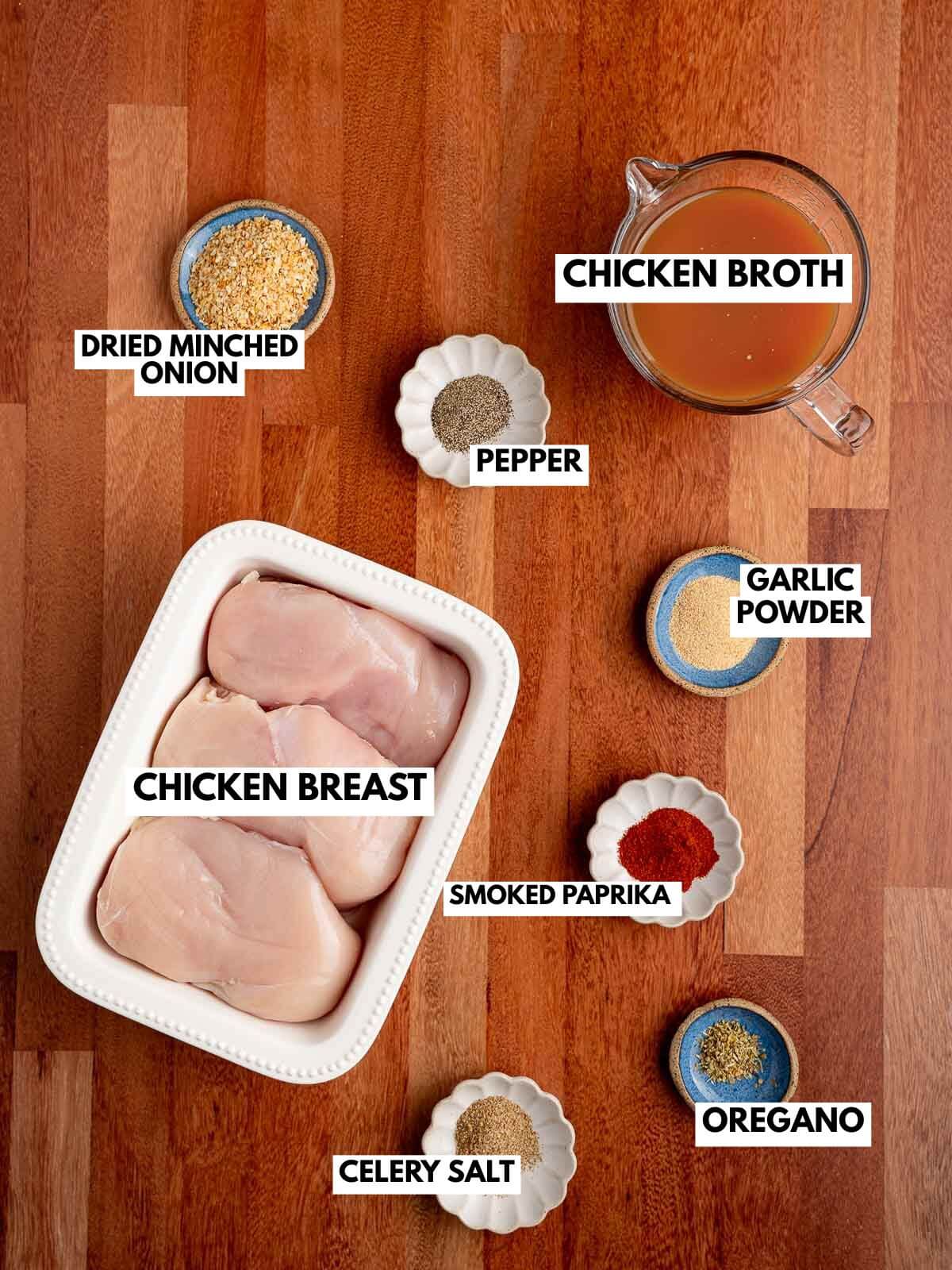 plate of uncooked chicken breast with bowls of spices and measuring cup full of broth.