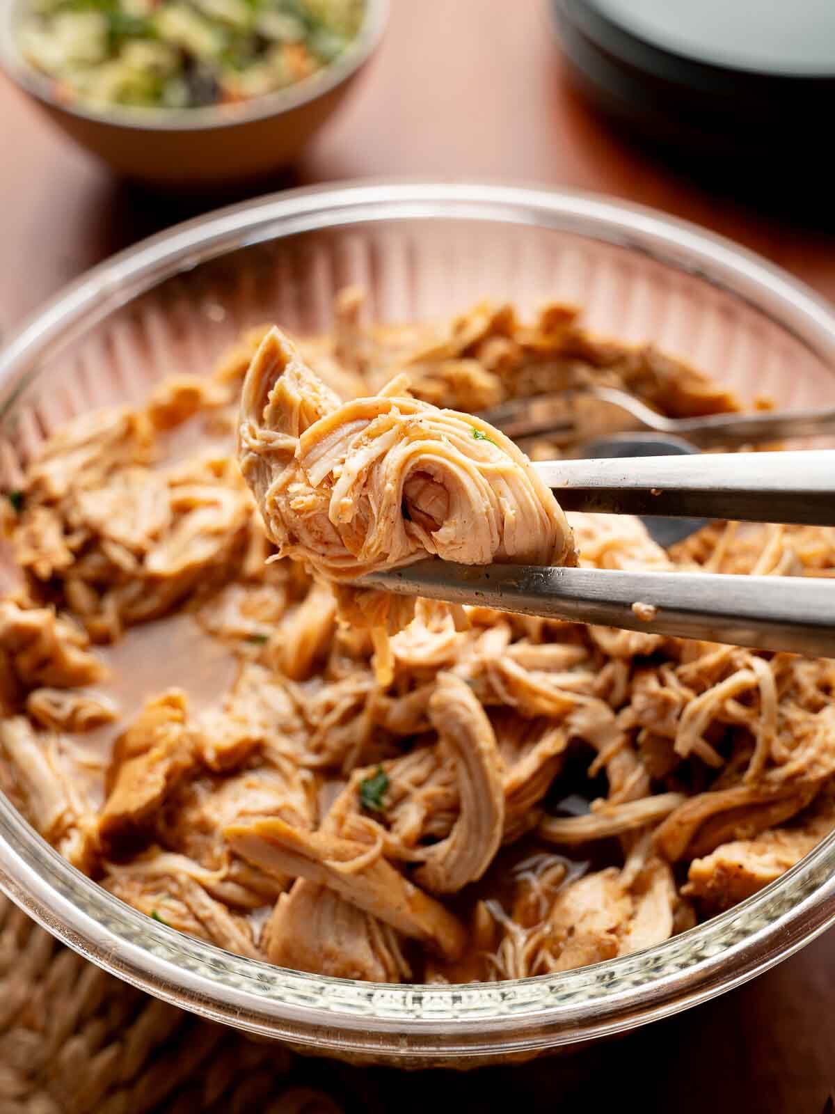shredded chicken in a bowl and a piece being held by tongs.