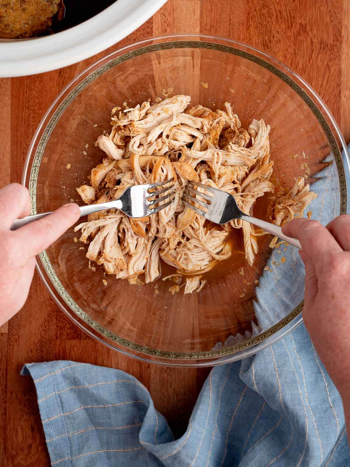 two hands shredding chicken in a bowl.