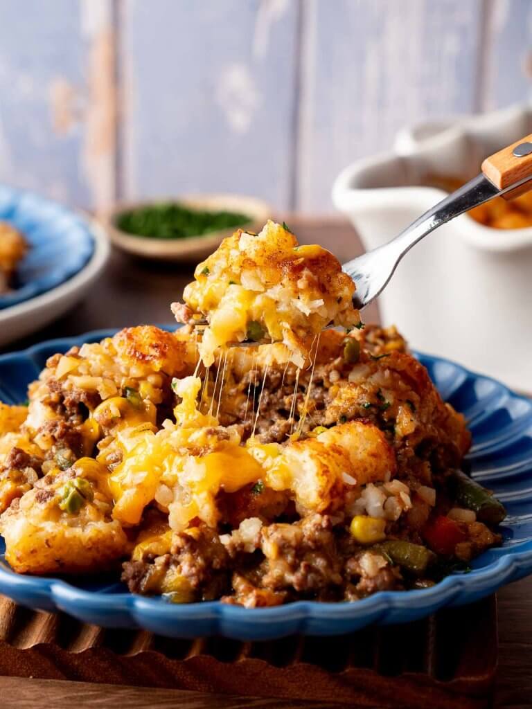 plate of cheesy tater tot casserole with a fork lifting up a big bite.