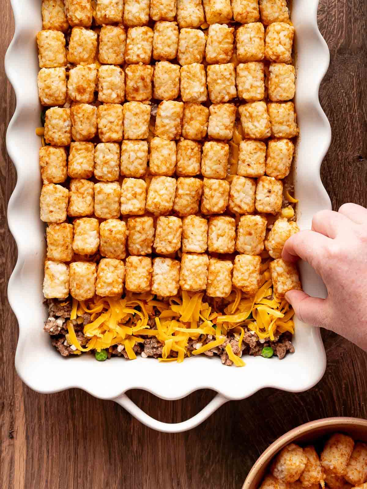 cheese and tater tots being added to casserole.