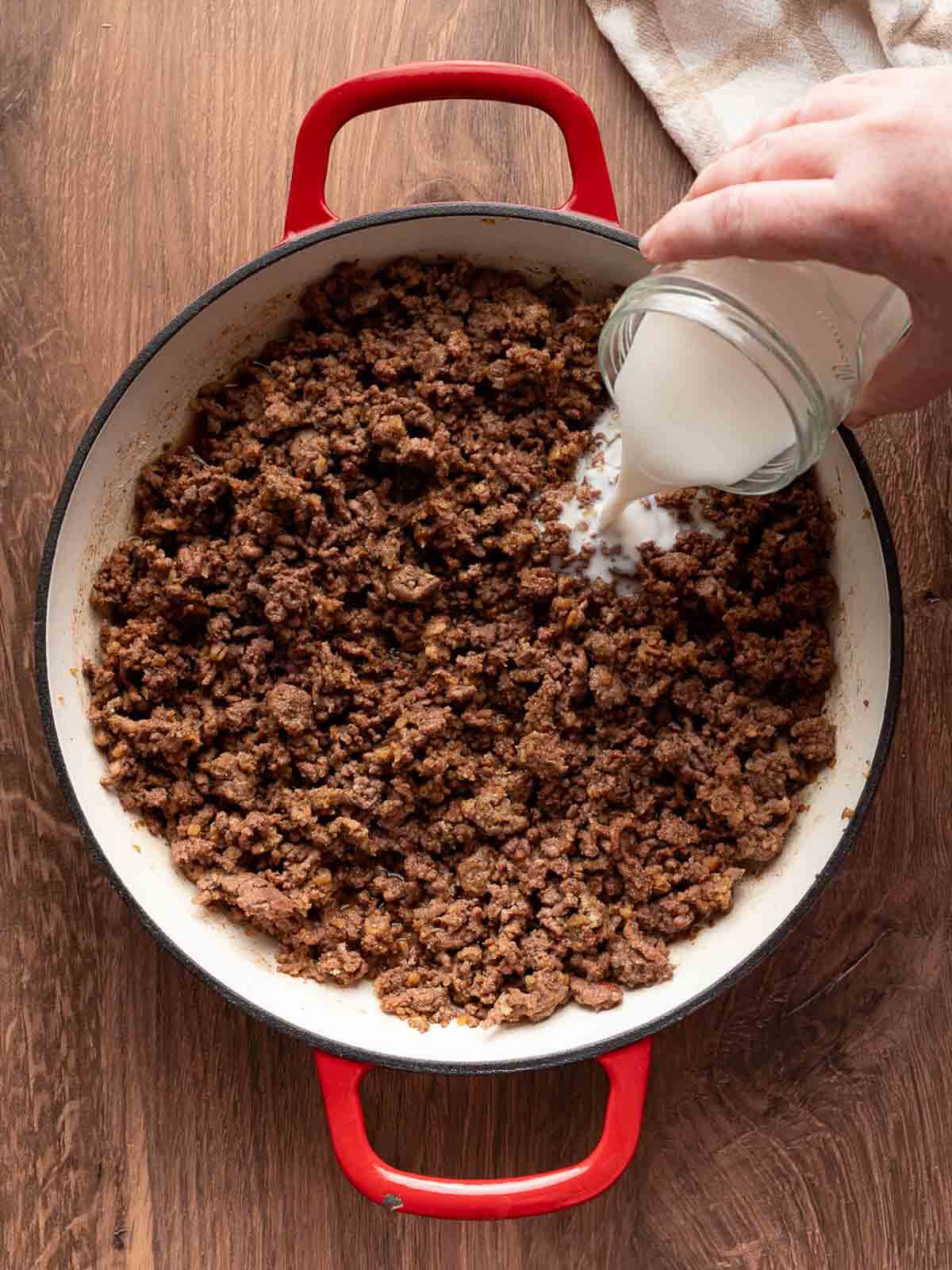 milk being poured onto the ground beef and flour.