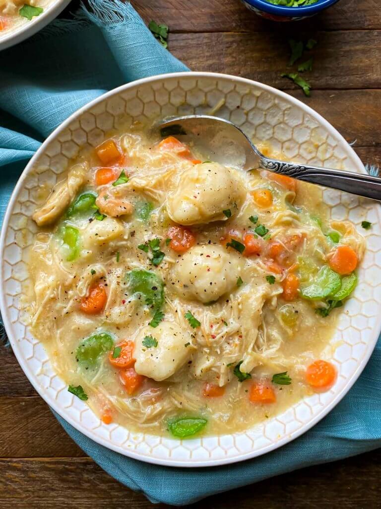 bowl of chicken and dumplingd with a spoon digging into it.